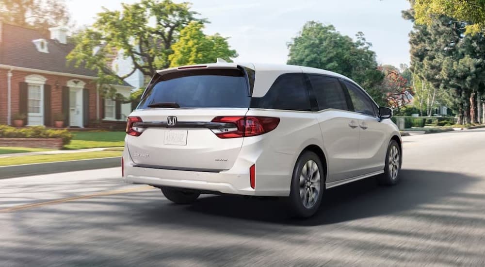 A white 2026 Honda Odyssey driving near a house.