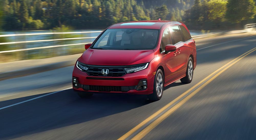 A red 2027 Honda Odyssey Elite driving by a lake.
