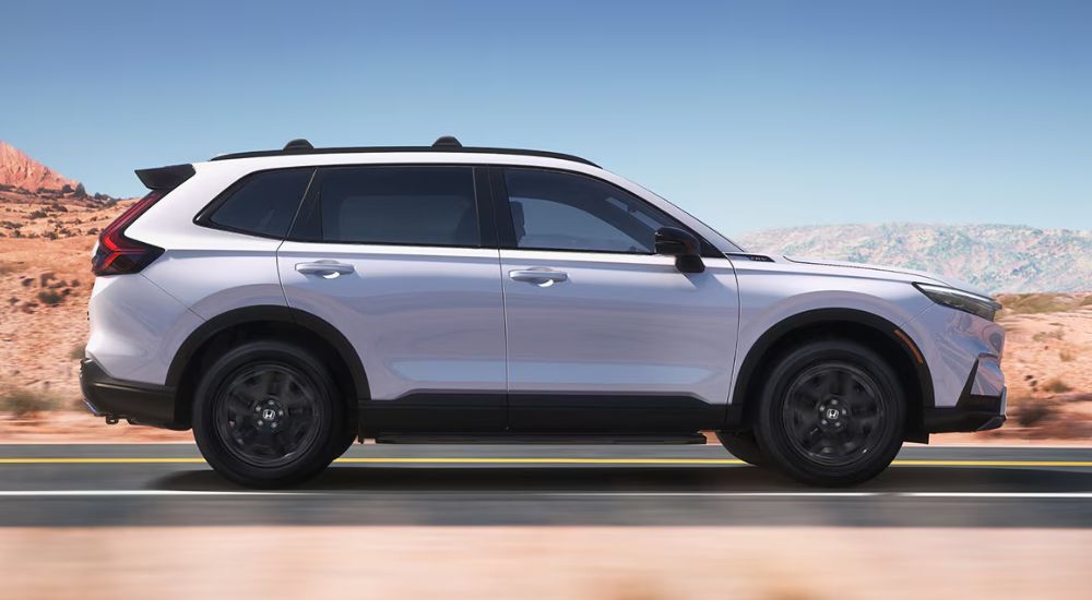 Side view of a white 2027 Honda CR-V Sport Touring Hybrid driving.