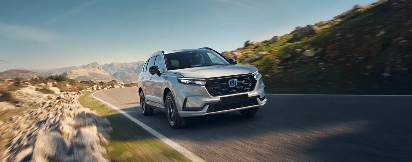A white 2025 Honda CR-V Hybrid driving a mountain road.