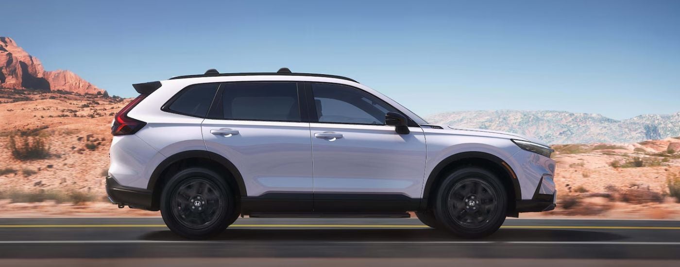 A white 2026 CR-V Hybrid driving on a paved road.