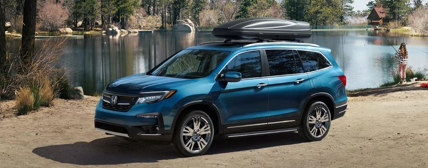 Blue 2020 Honda Pilot Elite parked off-road near a lake.