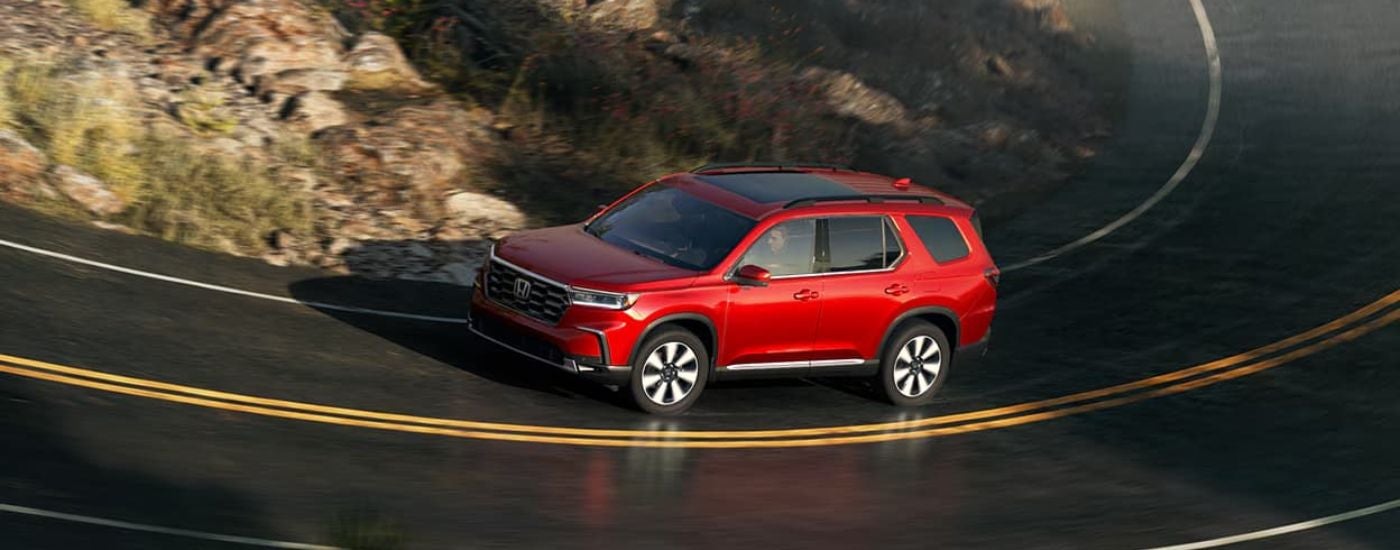 Red 2025 Honda Pilot driving around a bend.