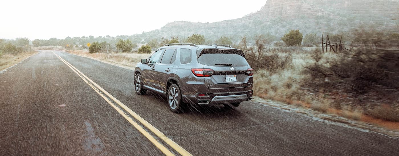 Rear of a silver 2025 Honda Pilot driving down a road.