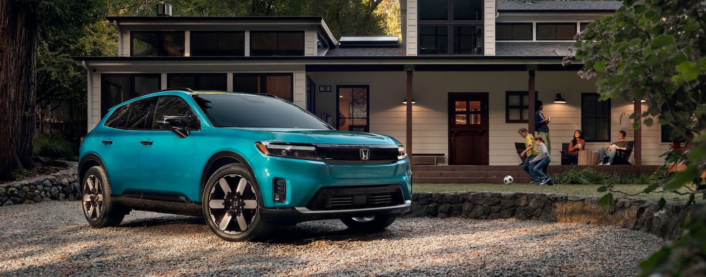 Blue 2026 Honda Prologue EV parked off-road in front of a house.