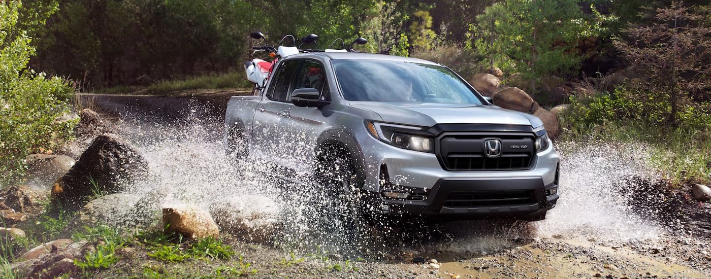 Silver 2025 Honda Ridgeline Sport driving off-road over a river.