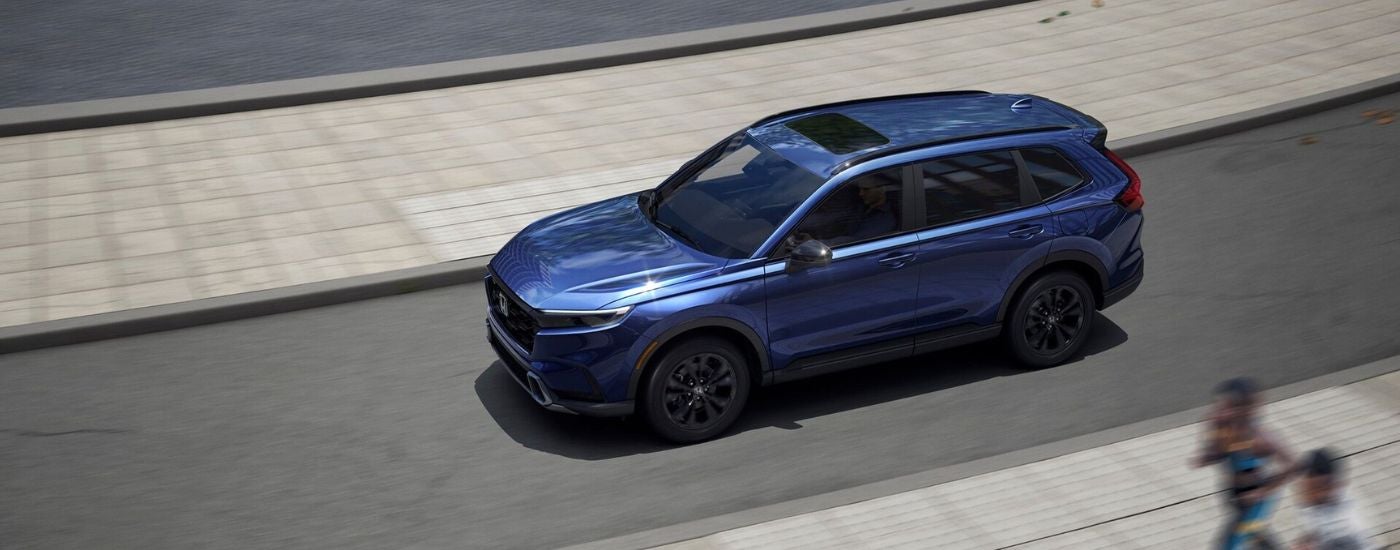Aerial view of a blue 2026 Honda CR-V Hybrid driving on a paved road.