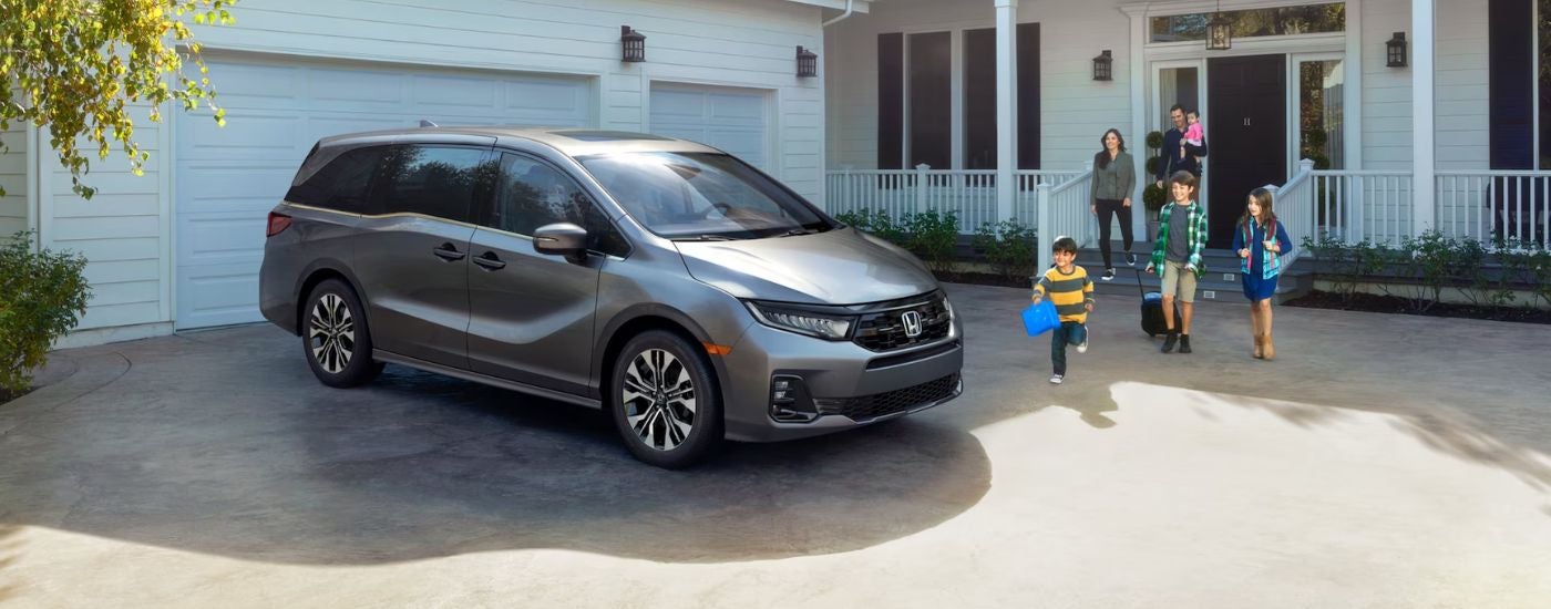 Grey 2026 Honda Odyssey parked in driveway with a family running to it.