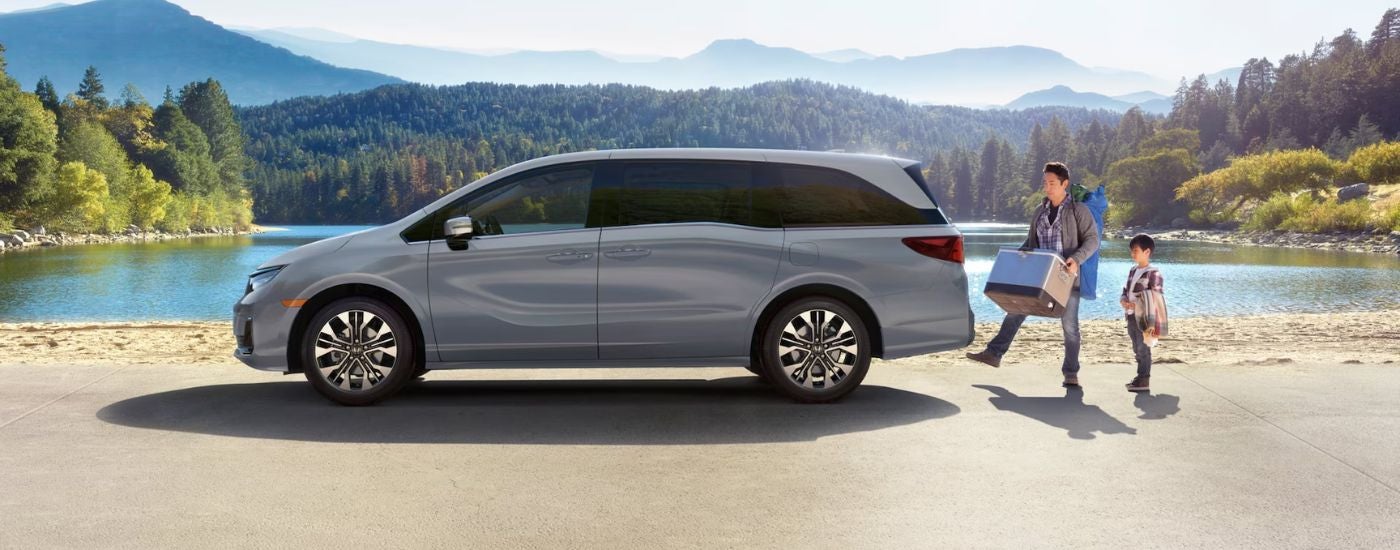 Grey 2026 Honda Odyssey parked near a lake with a man opening the cargo with his foot.
