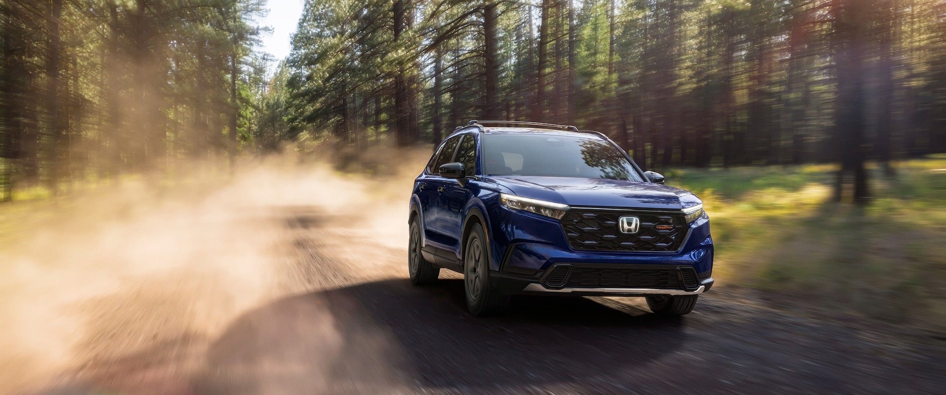 Blue 2026 Honda CR-V driving down a dirt road.