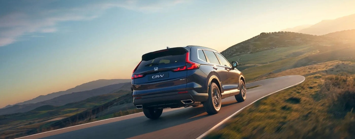Rear of a blue 2026 Honda CR-V Hybrid driving down a road.