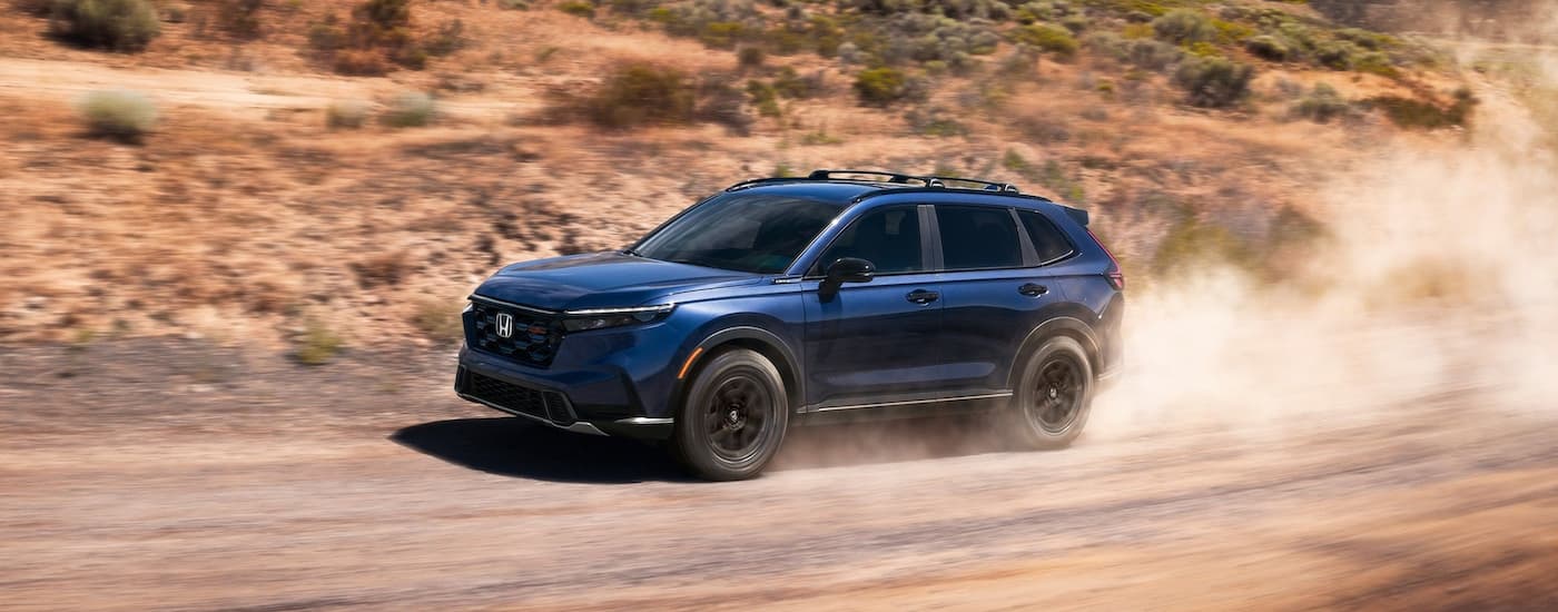 Dark blue 2026 Honda CR-V Hybrid driving on a dirt road.