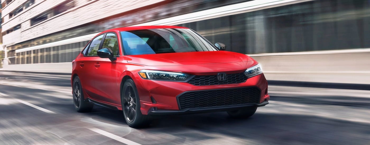 Red 2026 Honda Civic Sport driving down a road.