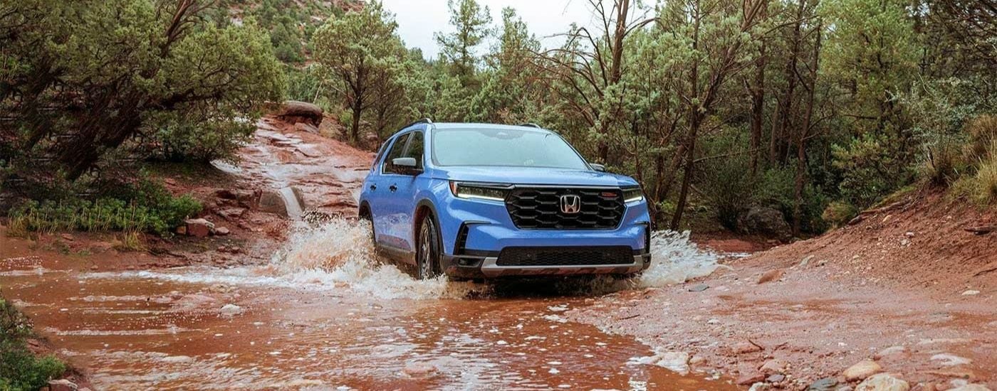 A blue 2023 Honda Pilot TrailSport driving through mud.