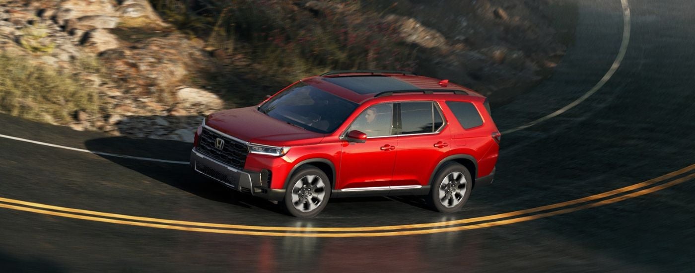 A red 2026 Honda Pilot shown driving a curvy paved road.